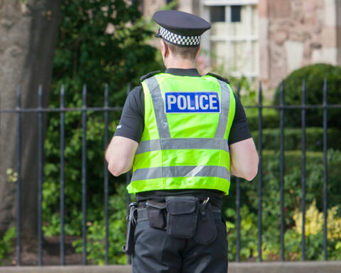 Police Scotland one office stands in street facing away from camera.