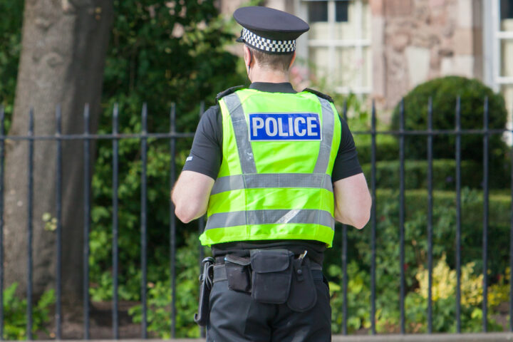 Police Scotland one office stands in street facing away from camera.