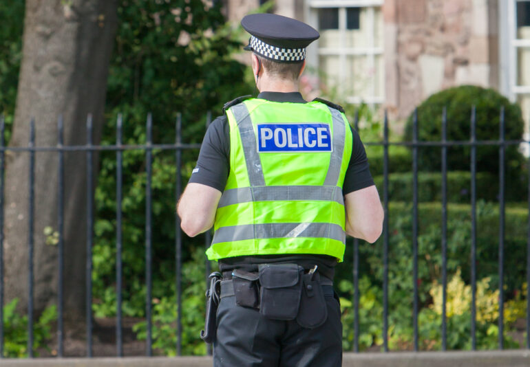 Police Scotland one office stands in street facing away from camera.