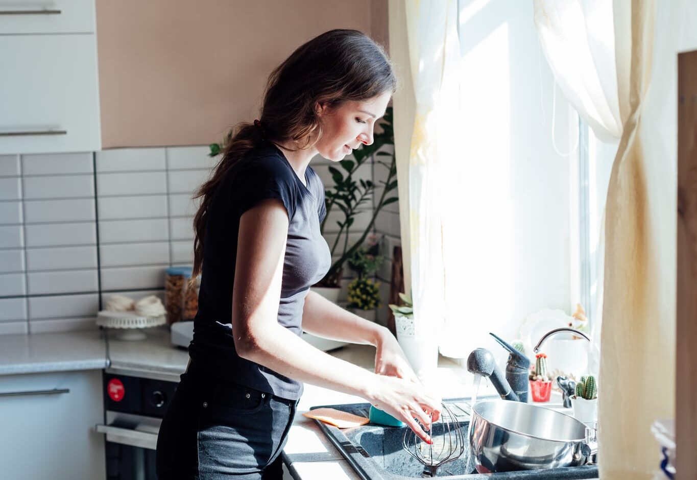 56149774 a housewife washes dishes in the kitchen in the sink by the window