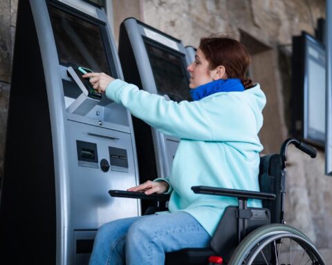 Caucasian woman in a wheelchair buys a train ticket using a mobile phone at a self service checkout