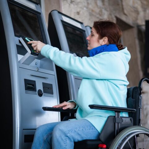 Caucasian woman in a wheelchair buys a train ticket using a mobile phone at a self service checkout