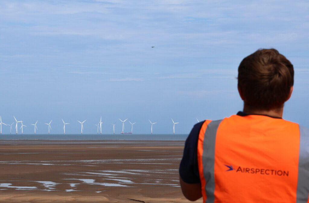 A drone flies towards an offshore wind farm monitored by an Airspection engineer
