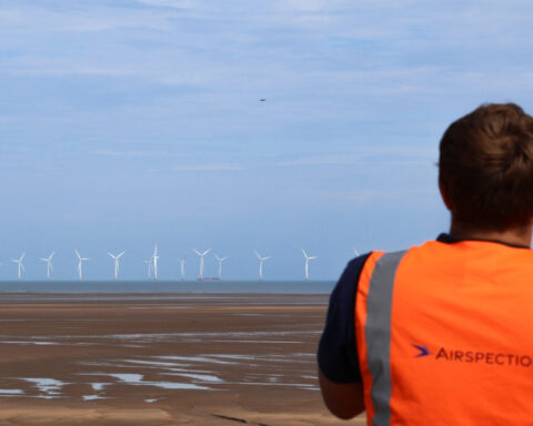 A drone flies towards an offshore wind farm monitored by an Airspection engineer