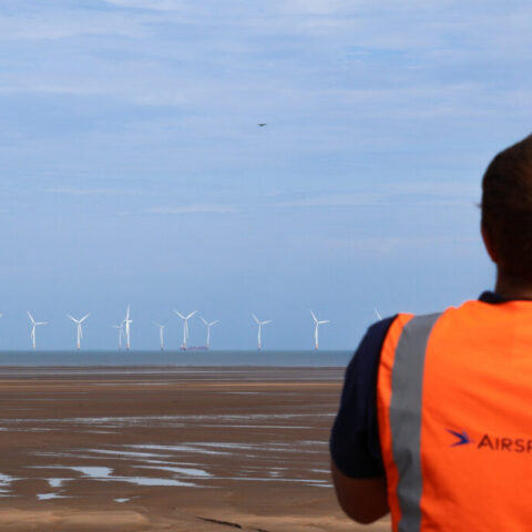 A drone flies towards an offshore wind farm monitored by an Airspection engineer